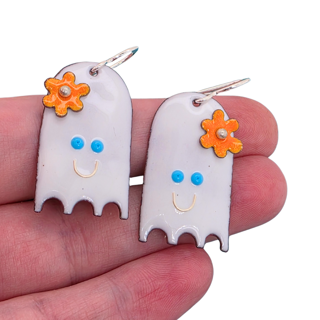 Ghost-shaped earrings with flower details held in a hand against a white background