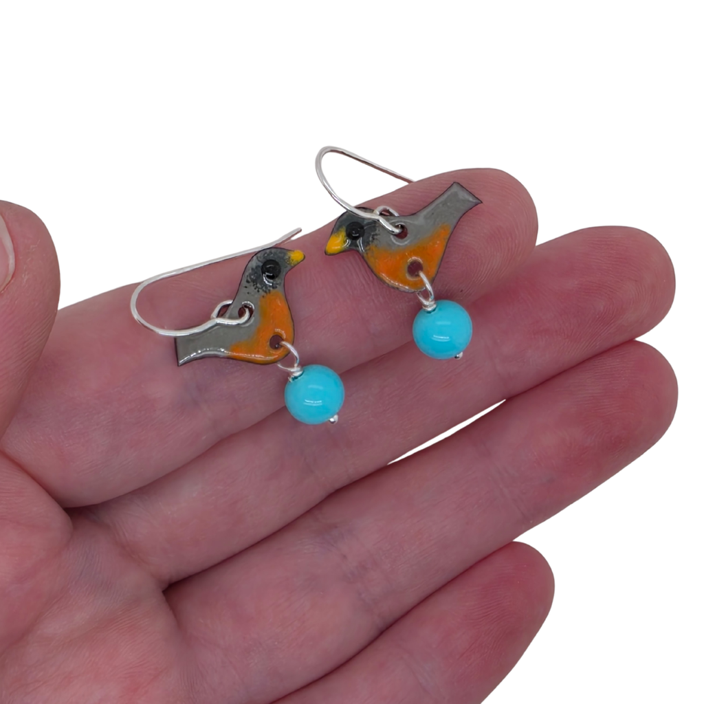Bird-shaped earrings with turquoise beads held in a hand on a white background