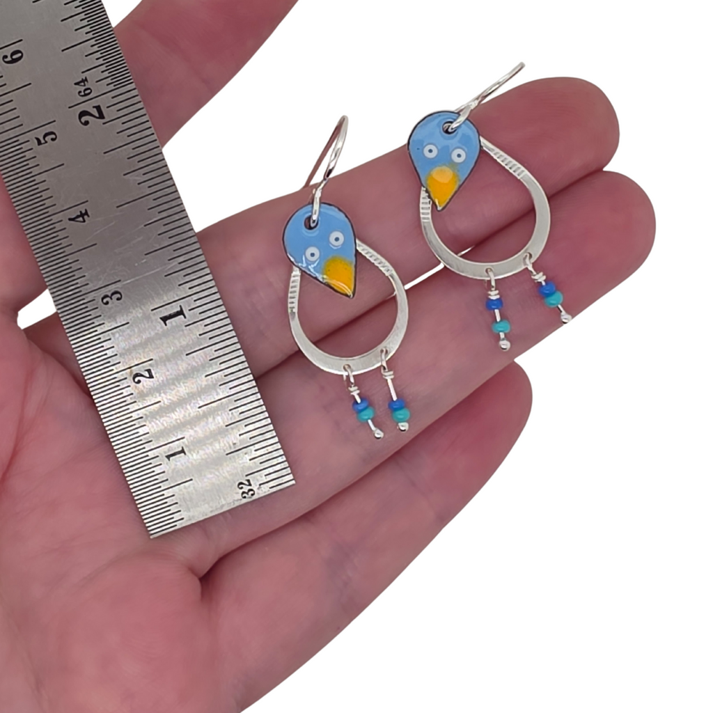 Bird-shaped earrings held in a hand with a ruler for scale.
