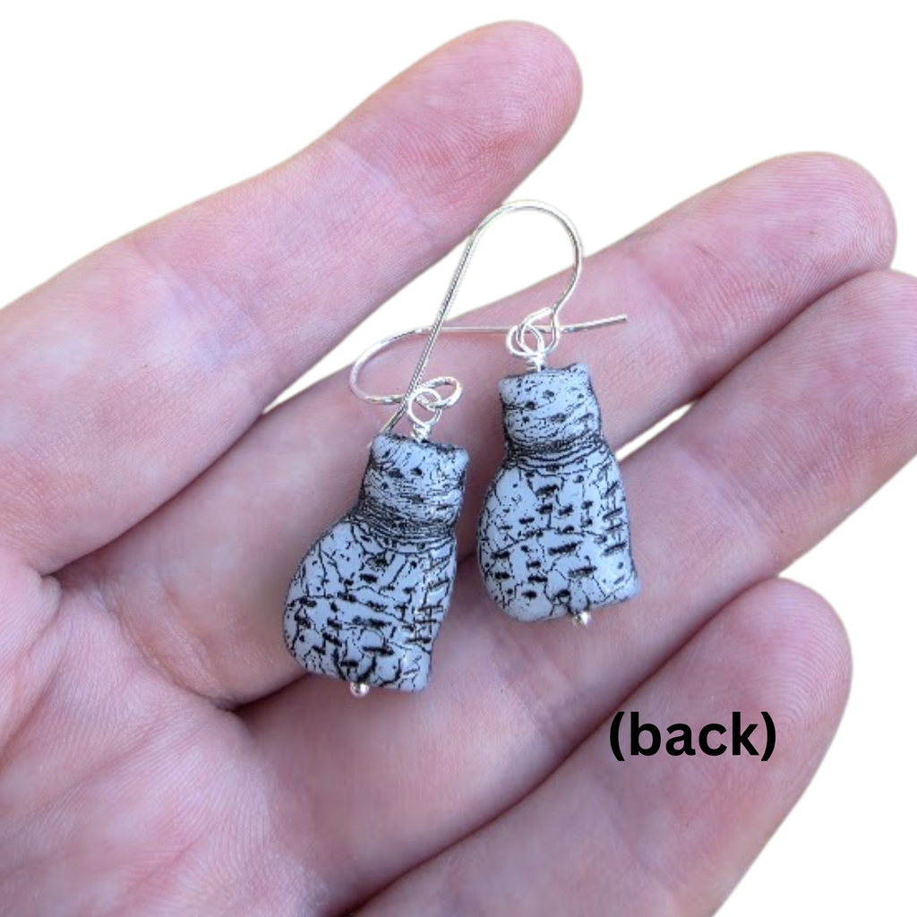 Pair of earrings on a hand with 'back' label showing the back of a pair of cat shaped earrings