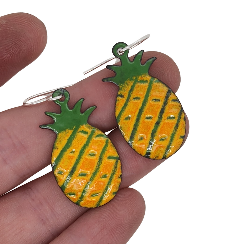 green, yellow, and orange pineapple earrings in hand for scale