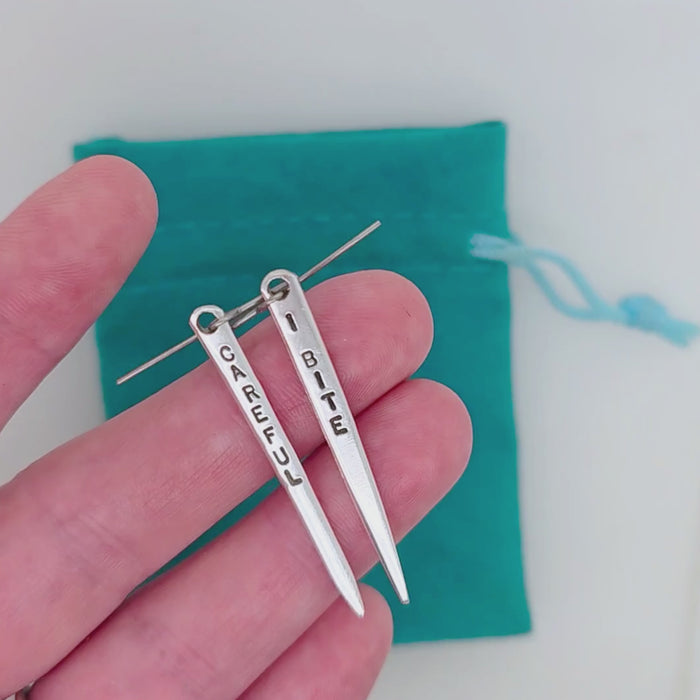 Handmade earrings crafted from upcycled and repurposed vintage silverplate fork tines.  One earring is stamped 'CAREFUL' and the other is stamped 'I BITE'.  Titanium earwires are at the top.  Made by artist Kathryn Riechert.